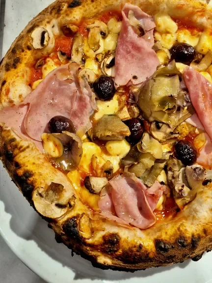 Pizza napolitana no Paesano Cuore Azzurro do Baxar Mercado, coberta com presunto de Parma, cogumelos Paris e shitake, e azeitonas pretas.